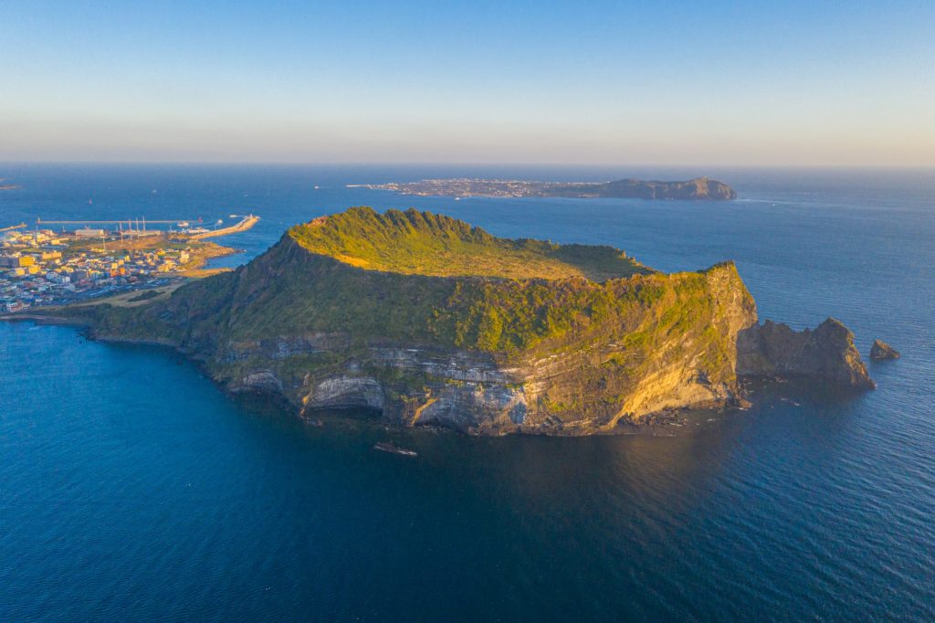Seongsan Ilchulbong: A sunrise view from the crater summit, with golden light spreading across the ocean and lush greenery.